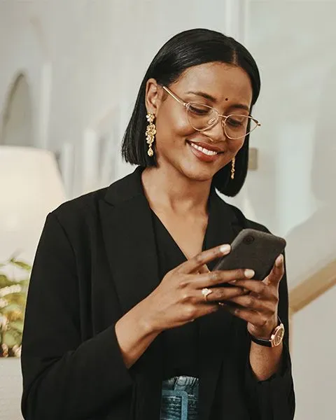 A physician, an East Indian woman wearing black professional clothes and a bindi, looking at her phone smiling.