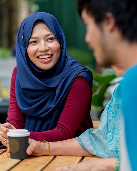 A woman smiling wearing a hijab talking with friend over coffee.