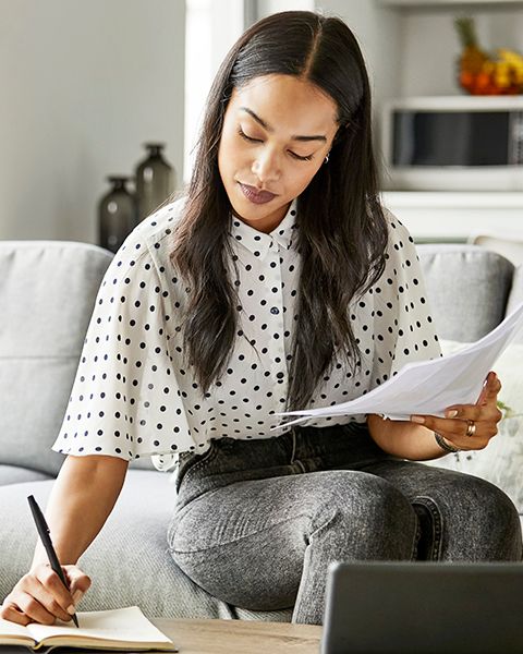 Indian physician, a woman at home sitting on her sofa dressed in a trendy polka dot shirt and jeans, comparing offer letters.